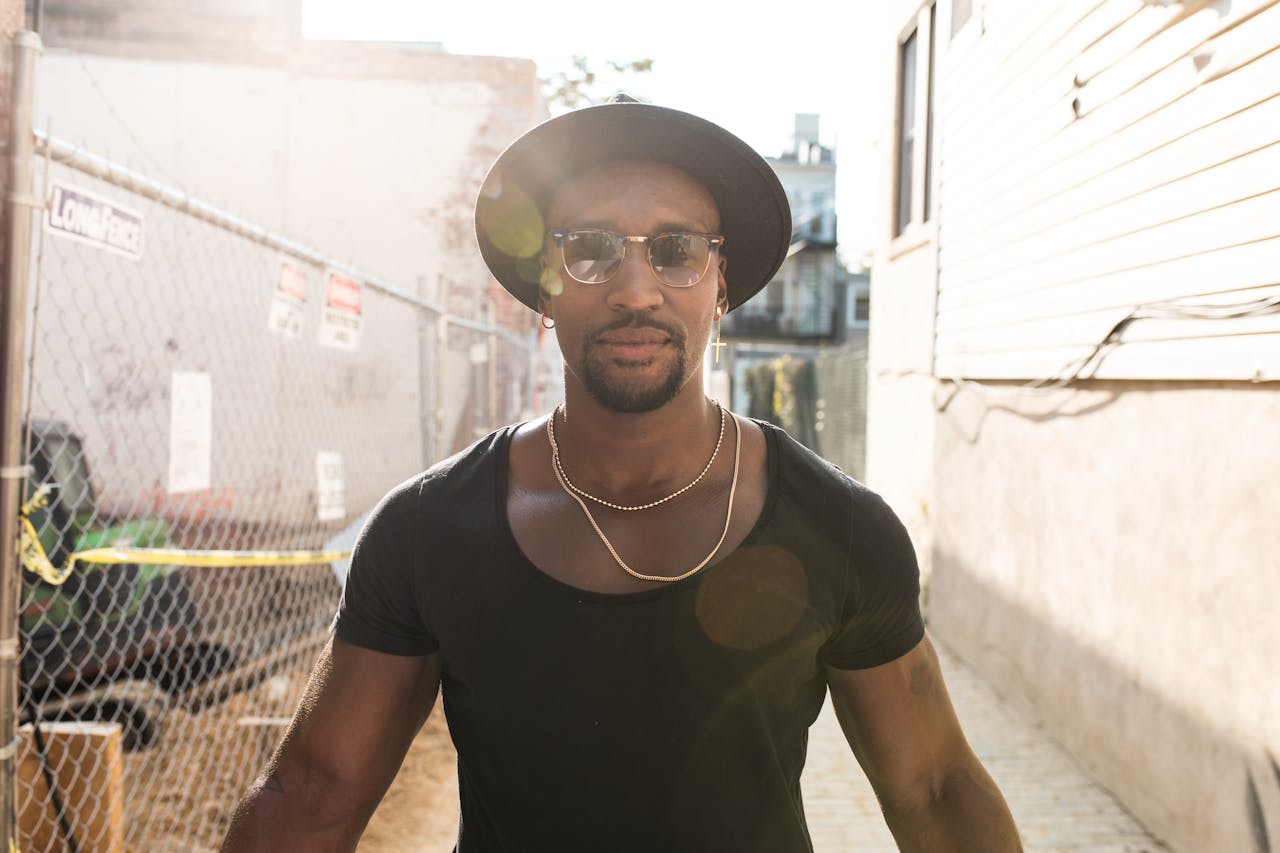 A fashionable man wearing sunglasses and a hat walking confidently on an urban street.